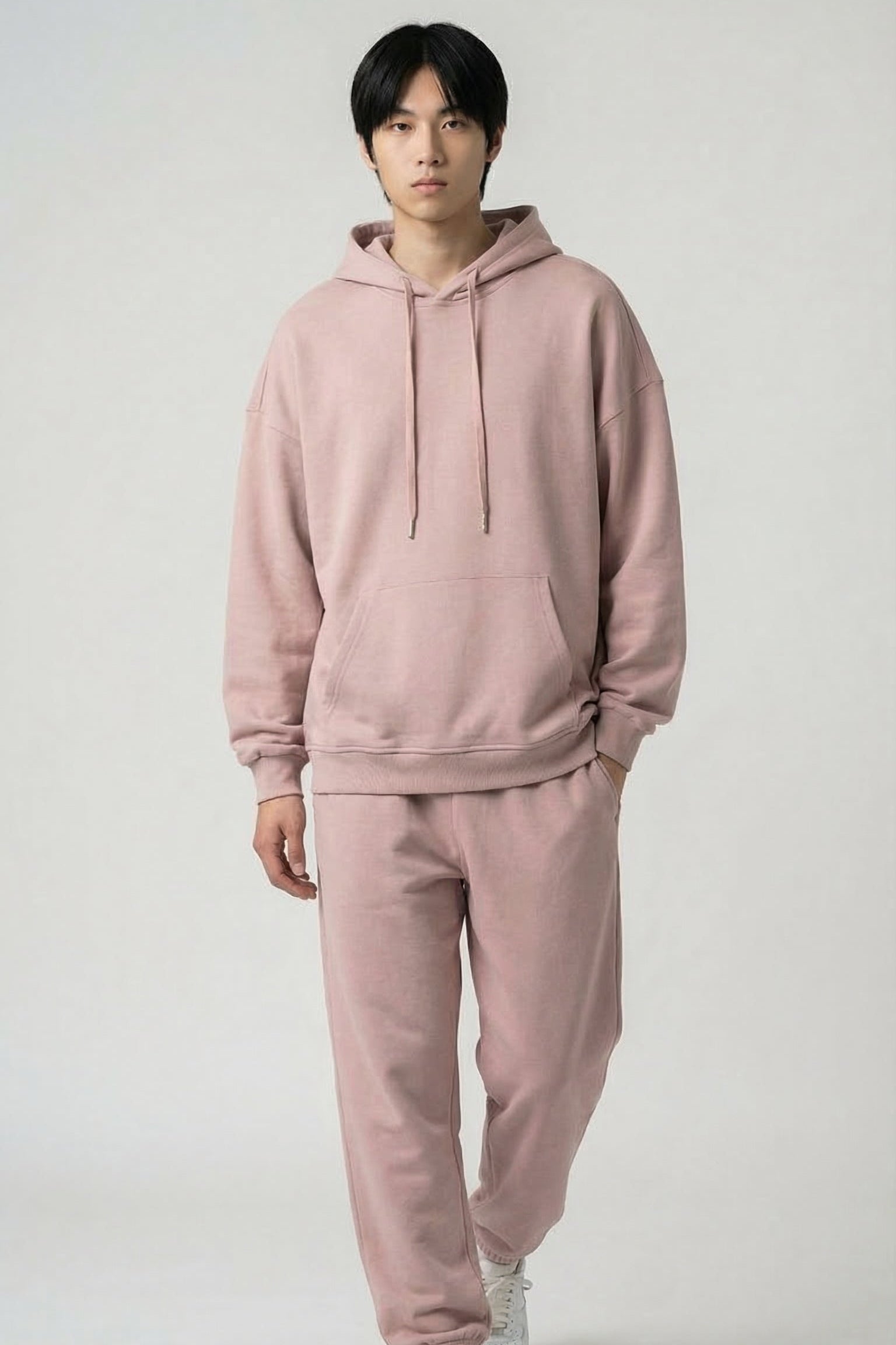 Person wearing a pink hoodie and pants set on a white background