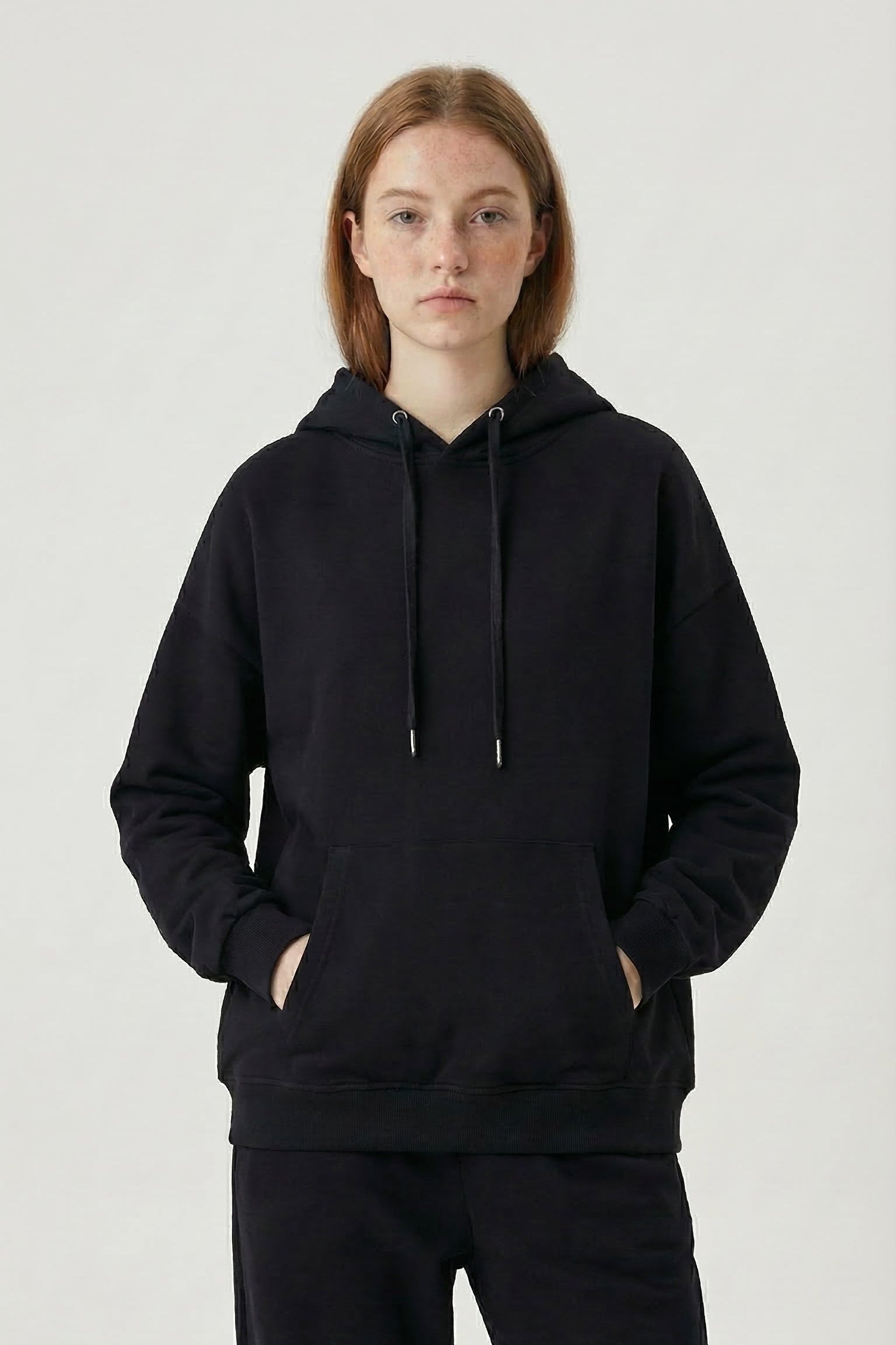 Person wearing a black hoodie and pants on a white background