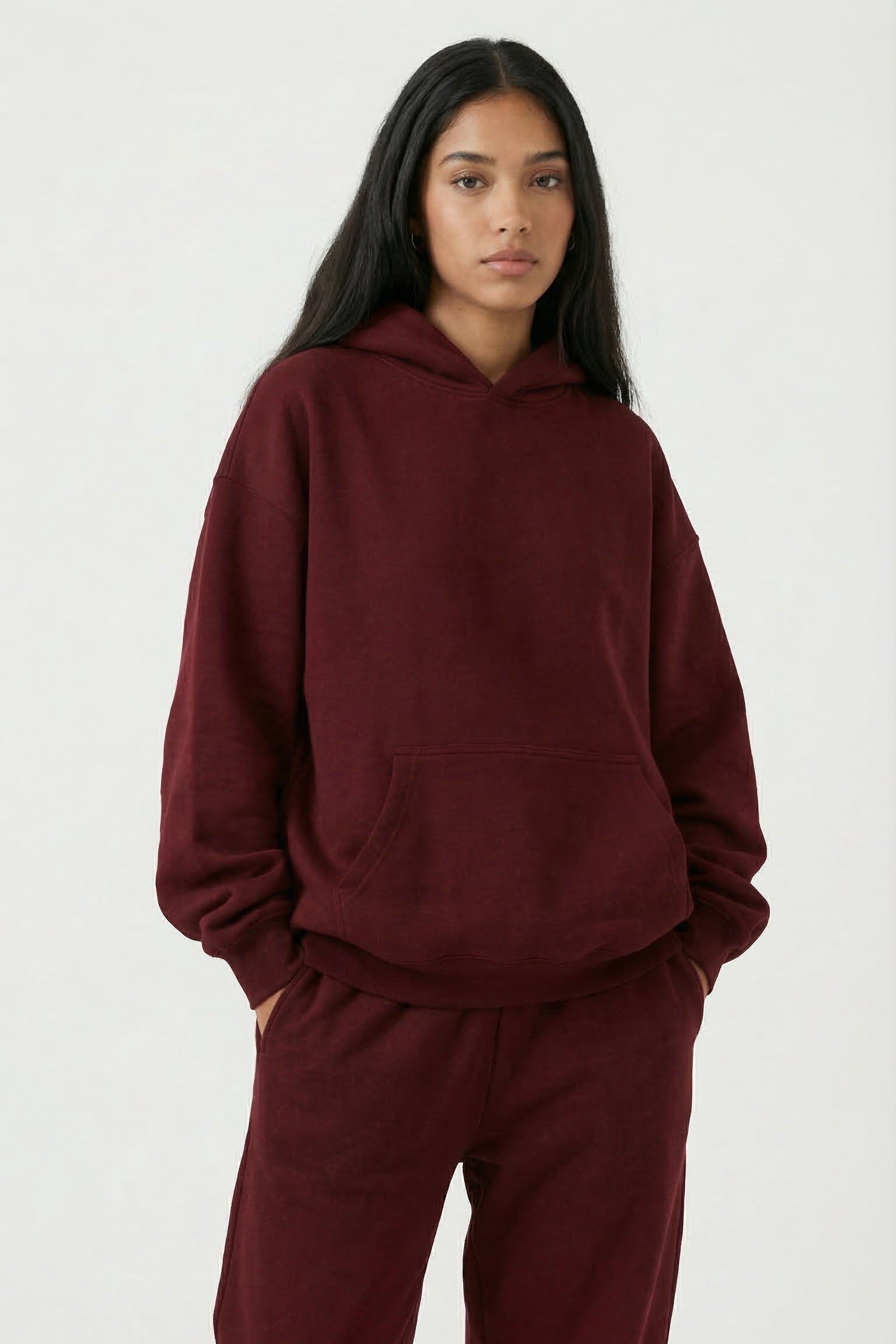 Person wearing a burgundy hoodie and pants on a white background