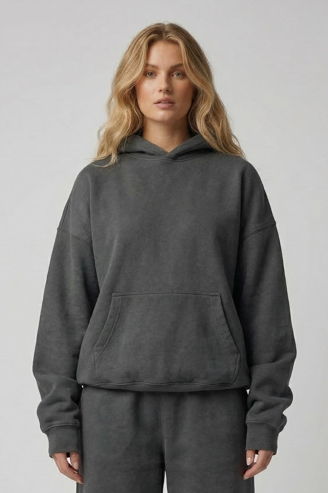 Person wearing a gray hoodie and pants set on a plain background