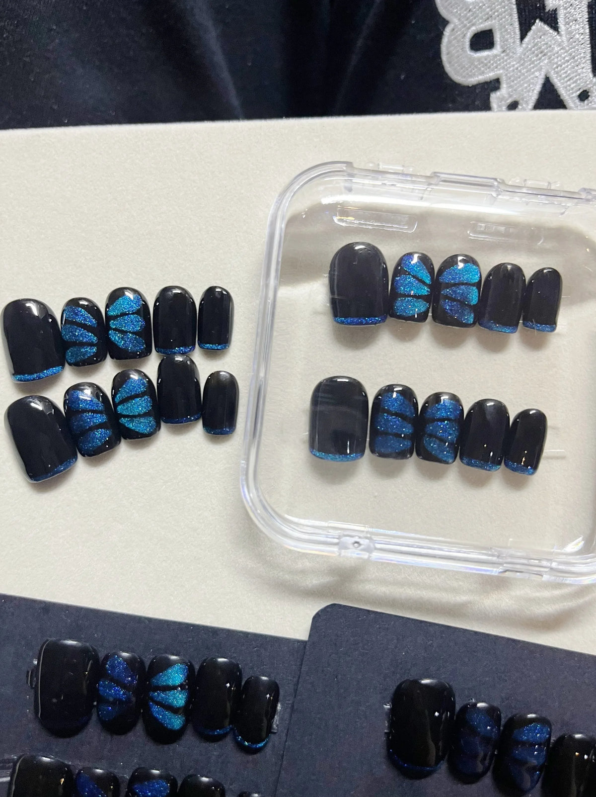 Press-on false nail set with dark navy tips and blue butterfly glitter, in clear case