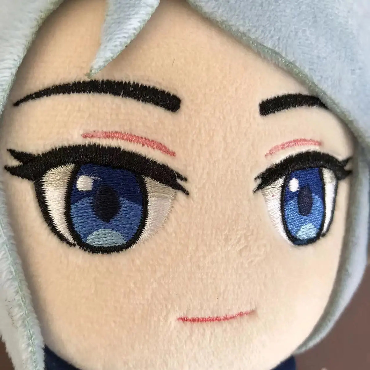 Close-up of light blue plush doll face with blue eyes and stitched smile