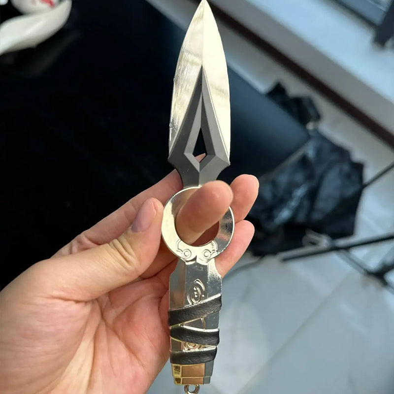 Kunai knife keychain held near ring, white blade and black handle with sheath loop