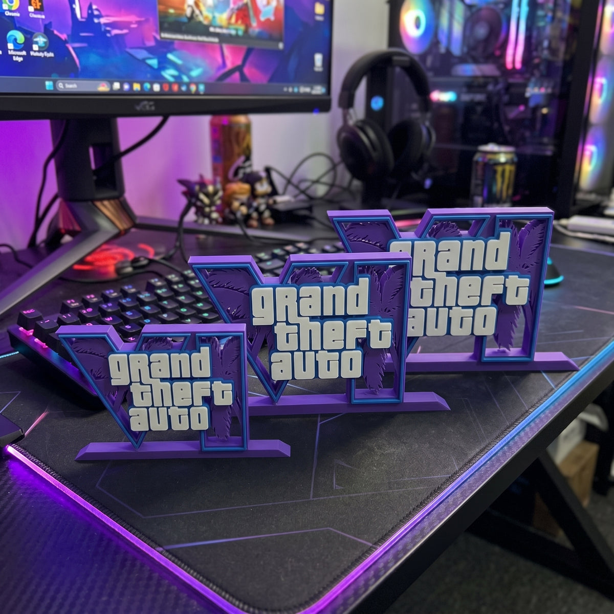 Three 3D-printed 'Grand Theft Auto' desk mats arranged on a gaming desk with a keyboard, mouse, headset, and computer monitor in the background.