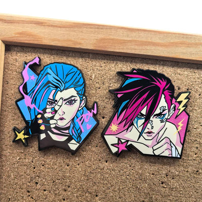 Two character enamel pins on cork backing, blue and magenta portraits