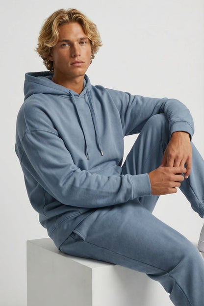 Person wearing a blue tracksuit sitting on a white block against a light gray background
