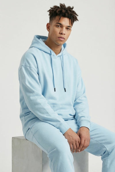 Person wearing a light blue hoodie and pants sitting on a concrete block.