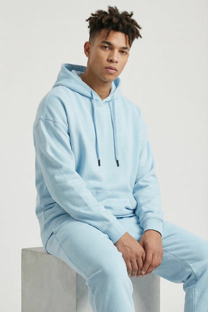 Person wearing a light blue hoodie and pants sitting on a concrete block.