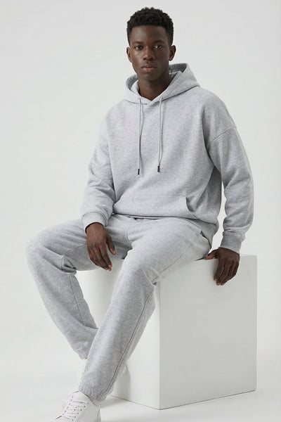Person wearing a gray tracksuit sitting on a white cube against a white background