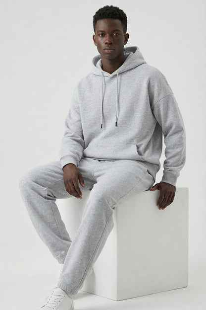 Person wearing a gray tracksuit sitting on a white cube against a white background