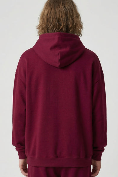 Person wearing a burgundy hoodie and pants on a white background