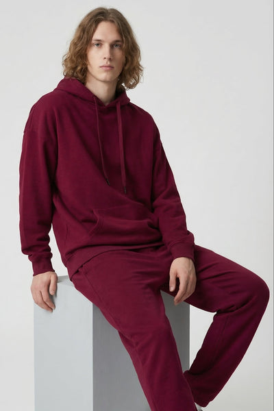 Person wearing a burgundy hoodie and pants sitting on a white block against a light gray background