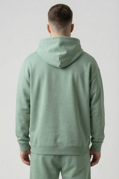 Person wearing a light green hoodie and pants on a plain background