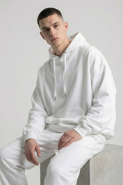 Person wearing a white hoodie and pants sitting on a white surface.