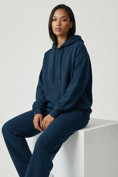 Person wearing a navy blue hoodie and pants sitting on a white cube against a light gray background