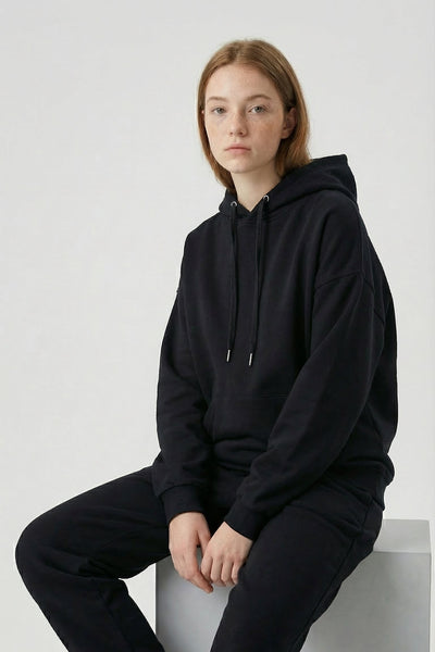 Person wearing a black hoodie and pants sitting on a white surface with a white background
