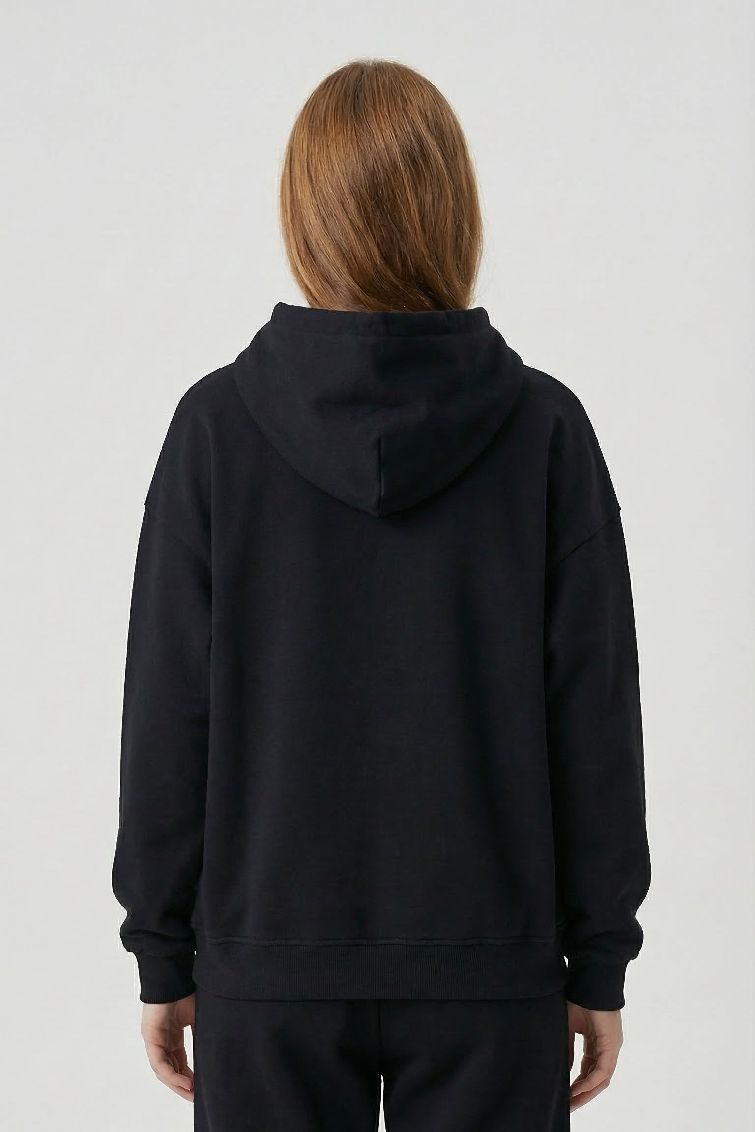 Person wearing a black hoodie and pants on a white background