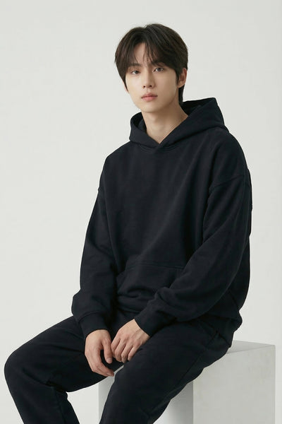 Person wearing a black hoodie and pants sitting on a white surface with a plain background
