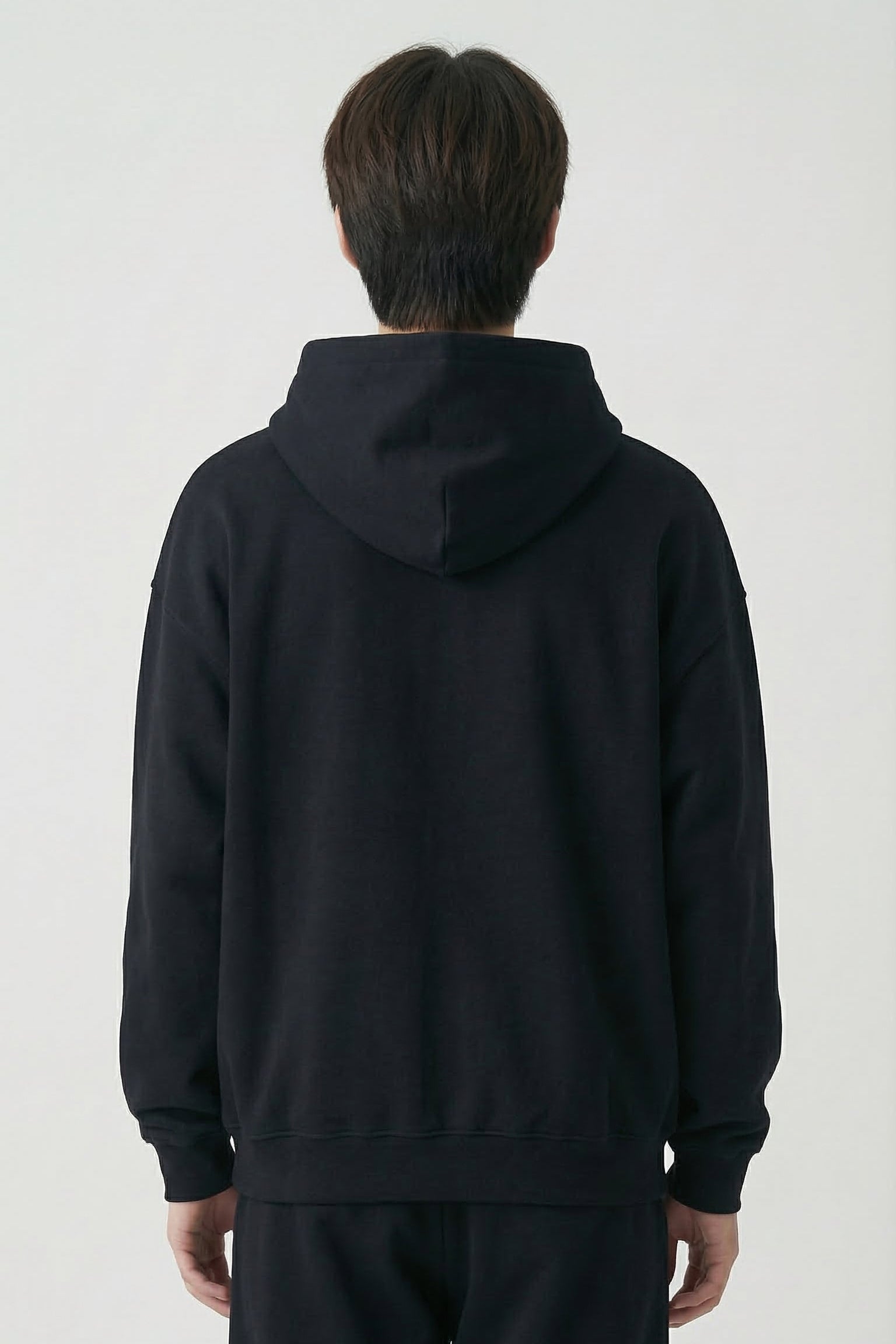 Person wearing a black hoodie and pants on a white background