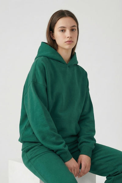 Person wearing a green hoodie and pants sitting on a white chair against a white background