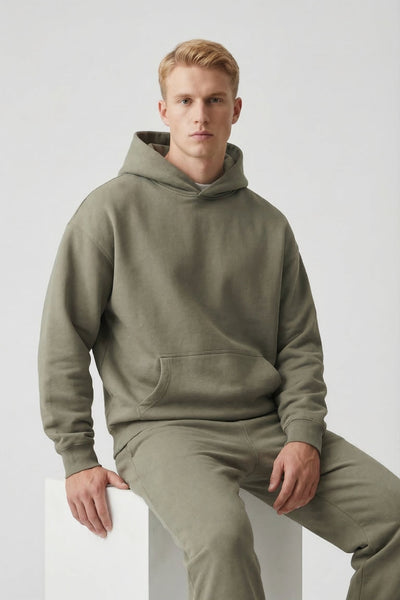 Man wearing a green hoodie and pants sitting on a white block against a light gray background