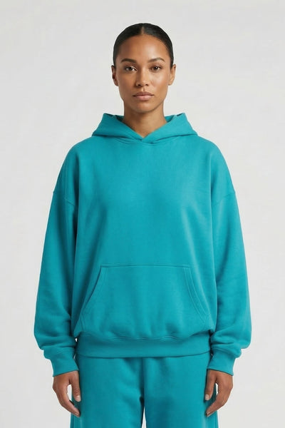Person wearing a teal hoodie and pants set on a white background