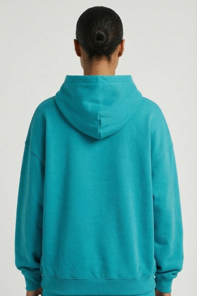 Person wearing a teal hoodie and pants on a light gray background