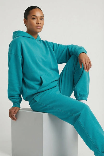 Person wearing a teal tracksuit sitting on a white cube against a light gray background