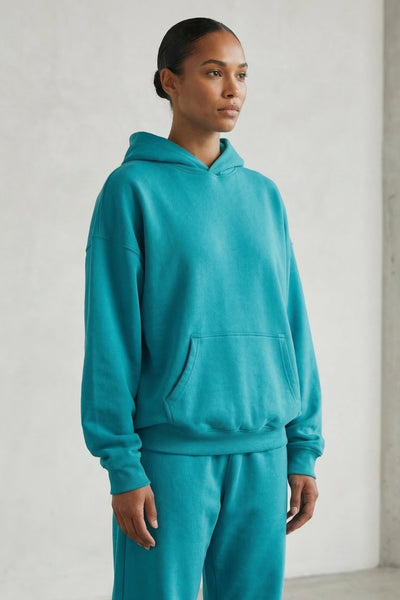 Person wearing a teal hoodie and pants against a plain background