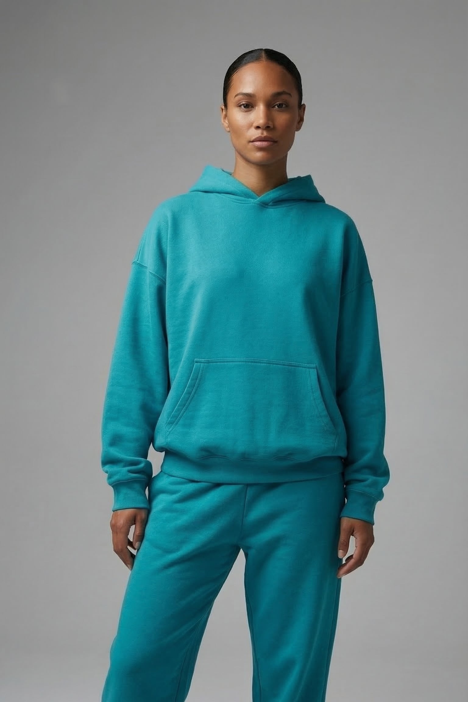 Person wearing a teal hoodie and pants on a gray background