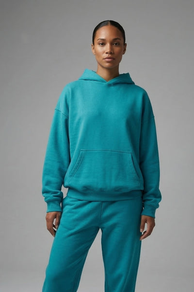 Person wearing a teal hoodie and pants on a gray background