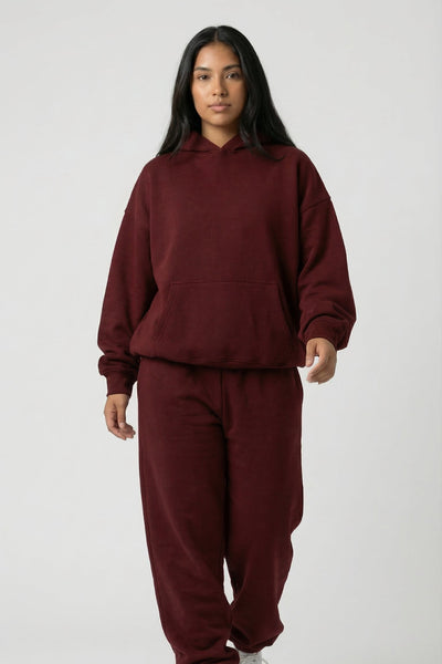 Person wearing a maroon tracksuit with white sneakers on a white background