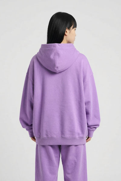 Person wearing a purple hoodie and pants set on a light gray background