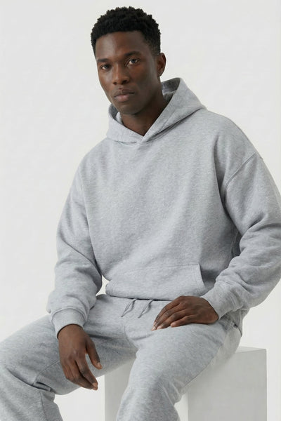 Person wearing a gray hoodie and sweatpants sitting on a white stool against a light gray background