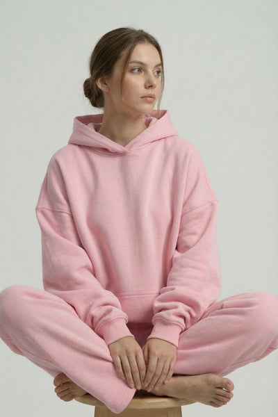 Person wearing a pink hoodie and pants sitting on a stool against a plain background