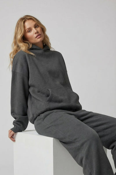 Woman wearing a dark gray sweatshirt and pants sitting on a white block against a light gray background
