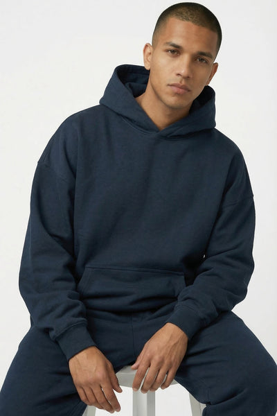 Man wearing a navy blue hoodie and pants sitting on a white stool against a light gray background