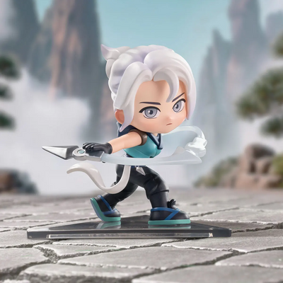 A chibi-style collectible figurine of a white-haired character in a dynamic pose, holding a silver blade, standing on a clear rectangular base against a blurred scenic background.