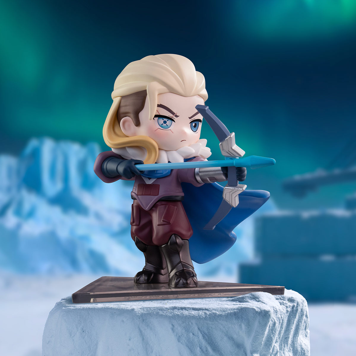 Sova A chibi-style collectible figurine of a blonde female archer character aiming a bow, posed on a snowy platform against a blurred icy blue background.