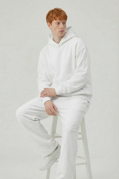 Person wearing a white hoodie and pants sitting on a stool against a plain background
