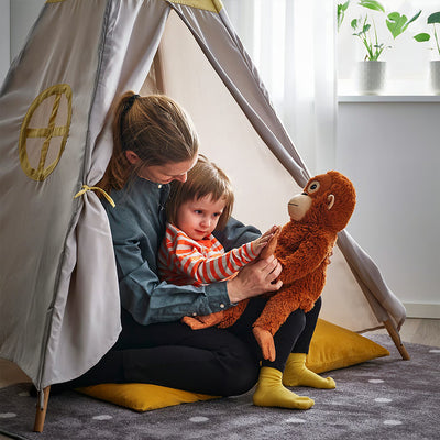 Brown plush monkey standing on floor with soft fur and friendly embroidered face