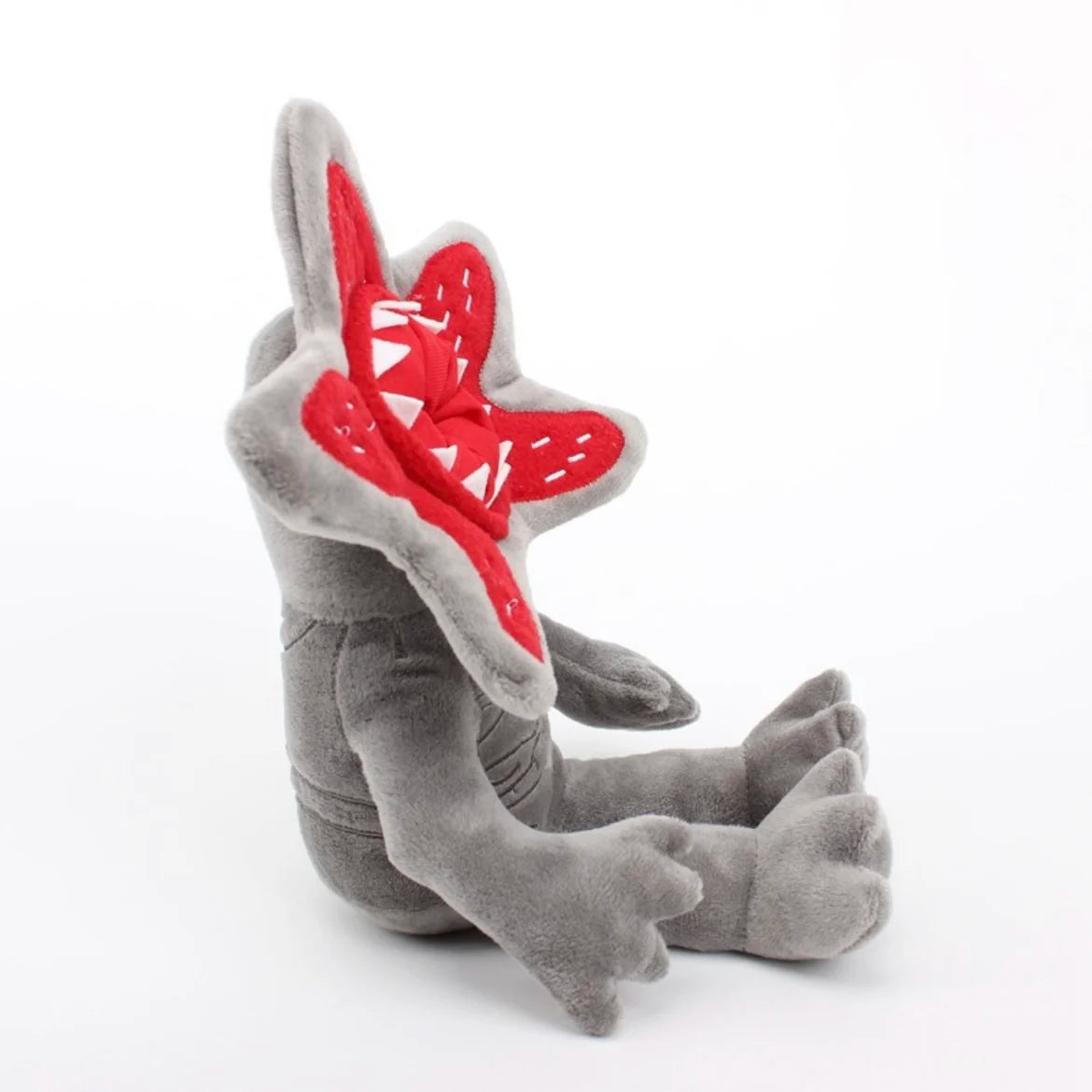 Gray plush character doll lying sideways with red star hood and stitched accents