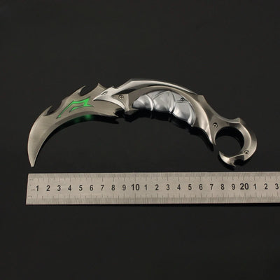 Karambit knife with silver blade and green accent markings, next to a ruler