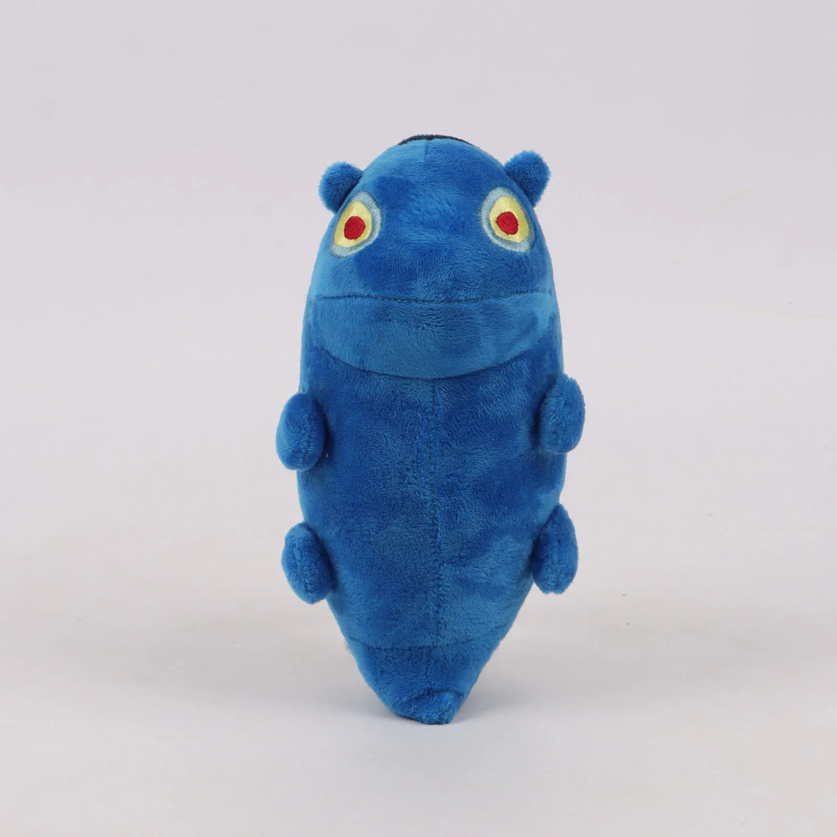 Blue plush toy standing upright with small arms and red-and-yellow eye emblems.