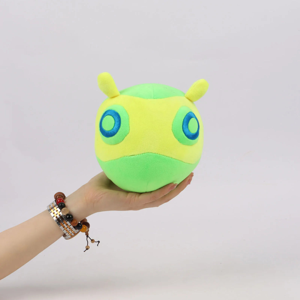 Green plush toy with yellow horns and blue eyes, held in a hand.