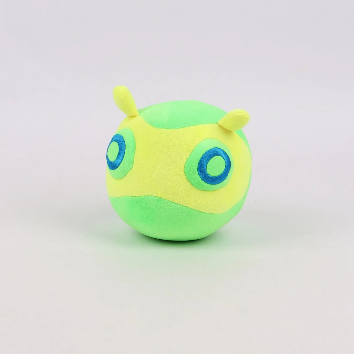 Green round plush toy with small yellow horns and blue circular eyes.